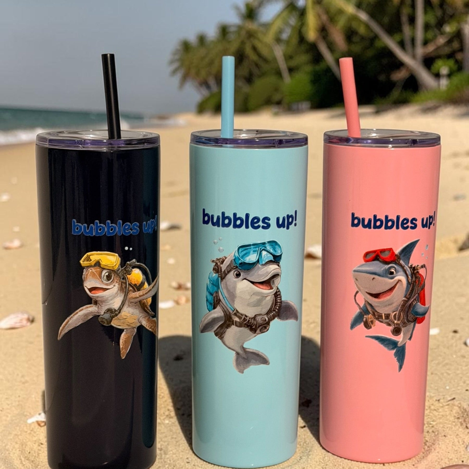 Three insulated tumblers with shark designs and 'bubbles up!' text on a beach.